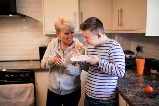 Teenage boy eating toast with a foster carer in her kitchen